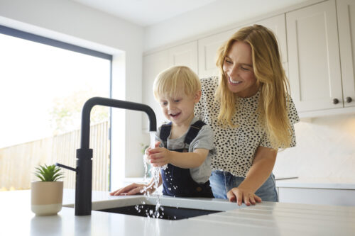 Mother With Son At Home In Kitchen Washing Hands In Sink Or Basin Together